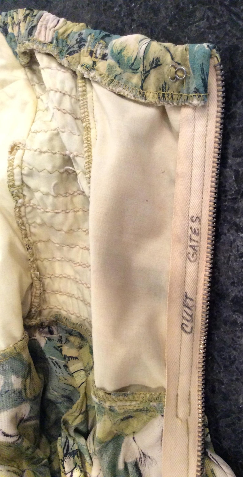 May include: Close-up of the inside of a garment with a floral print. The zipper is visible and has the text "COUTT GATES" printed on it.