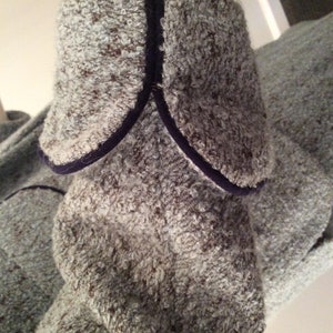 May include: Close-up of a blue and gray sweater with a dark blue trim around the collar and cuffs.