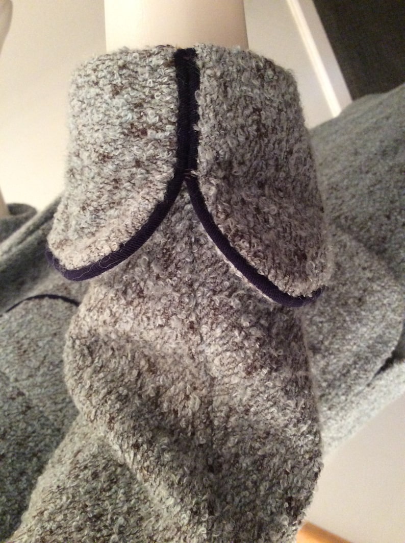 May include: Close-up of a blue and gray sweater with a dark blue trim around the collar and cuffs.