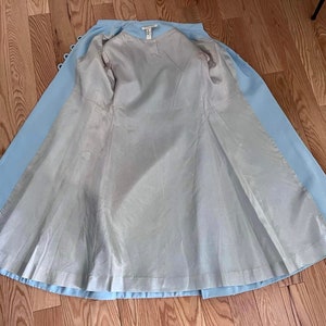 May include: A light blue coat with a white lining. The coat is open and the lining is visible. The coat has a button closure and a long, flowing skirt.