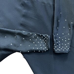 May include: Black long-sleeved dress with a subtle textured fabric and a dotted pattern on the sleeves. The dots are made of small, white rhinestones.