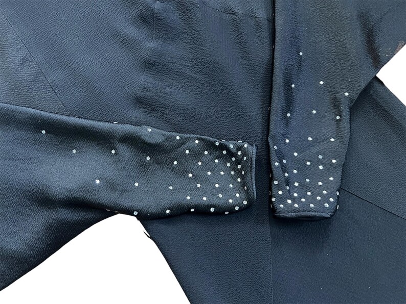 May include: Black long-sleeved dress with a subtle textured fabric and a dotted pattern on the sleeves. The dots are made of small, white rhinestones.