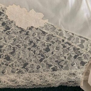 May include: White satin fabric with a lace trim. The lace is a delicate floral pattern with a scalloped edge.