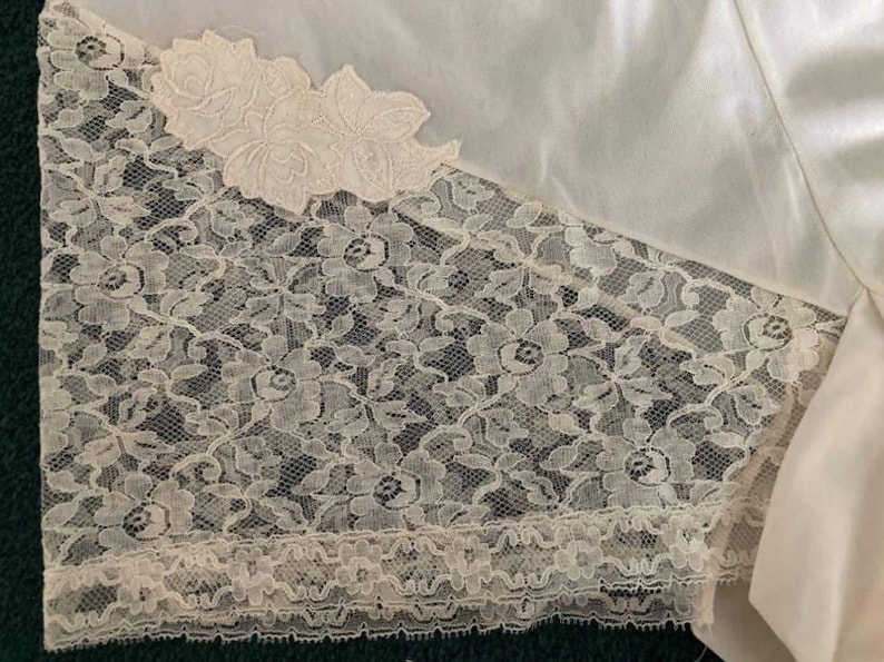 May include: White satin fabric with a lace trim. The lace is a delicate floral pattern with a scalloped edge.