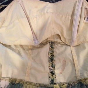 May include: The inside of a white dress with a green and yellow floral print. The dress has a built-in bra and a zipper in the back. The label says "Best 2" and "South Korea".