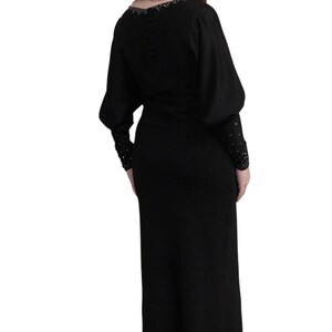 May include: A black maxi dress with long sleeves and a beaded neckline. The dress has a fitted bodice and a flowing skirt.
