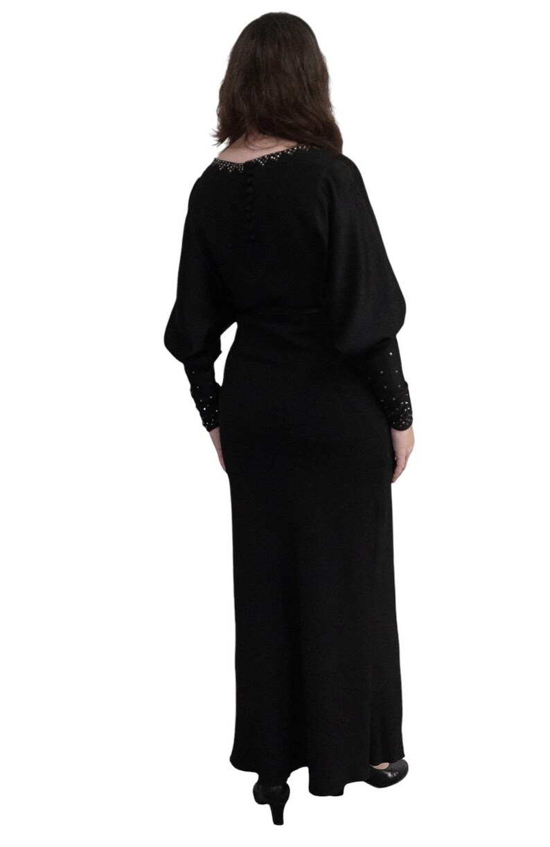 May include: A black maxi dress with long sleeves and a beaded neckline. The dress has a fitted bodice and a flowing skirt.