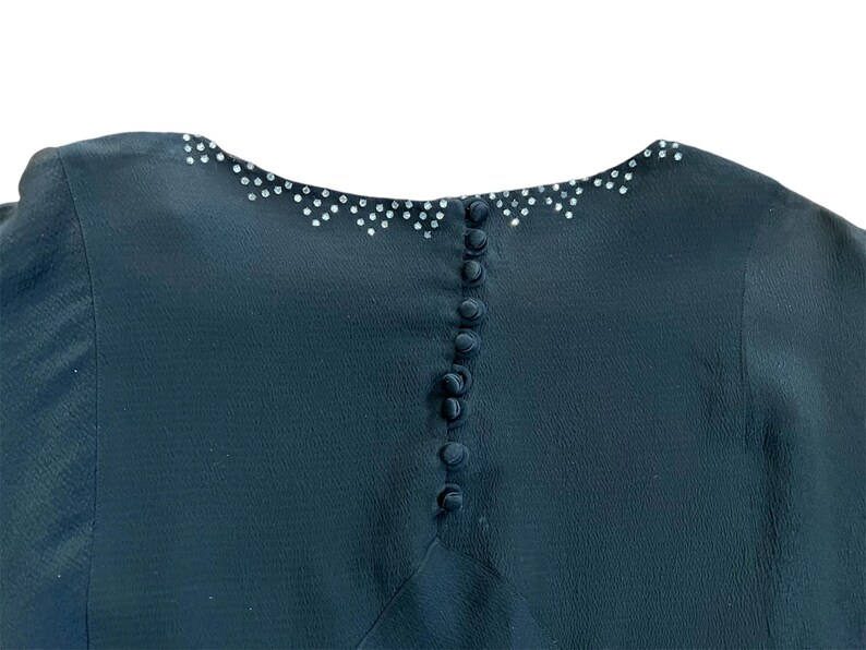 May include: A black dress with a row of buttons down the back and a sparkly trim around the neckline.