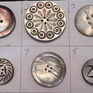 May include: Eight round, white mother-of-pearl buttons with various designs. The buttons are numbered 1 through 8.