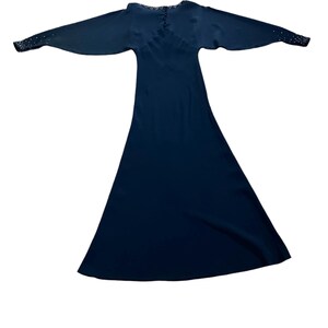 May include: A long, dark blue dress with a V-neckline and long sleeves. The sleeves have a row of small, white embellishments at the cuffs.