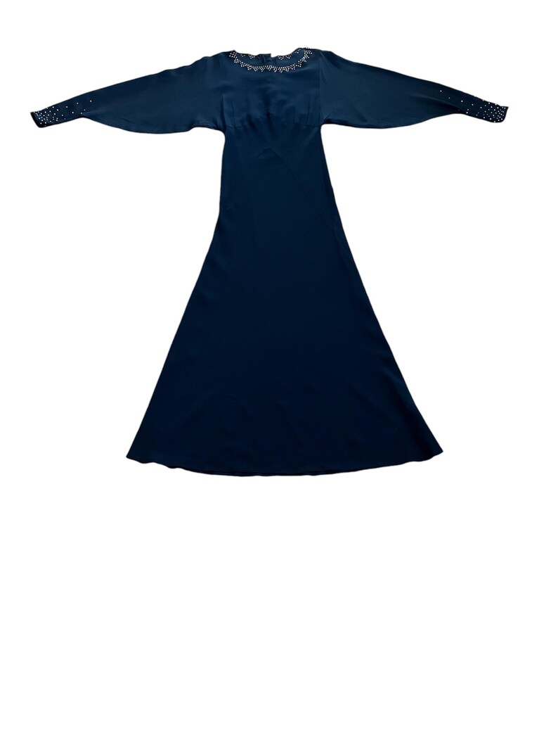 May include: A long, dark blue dress with a beaded neckline and long sleeves. The dress has a fitted bodice and a flowing skirt.