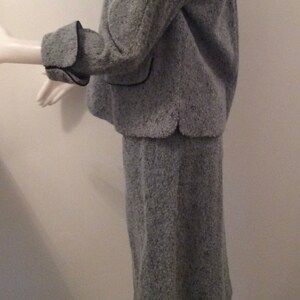 May include: A gray tweed skirt suit with black trim. The jacket has a collar and long sleeves. The skirt is knee-length.