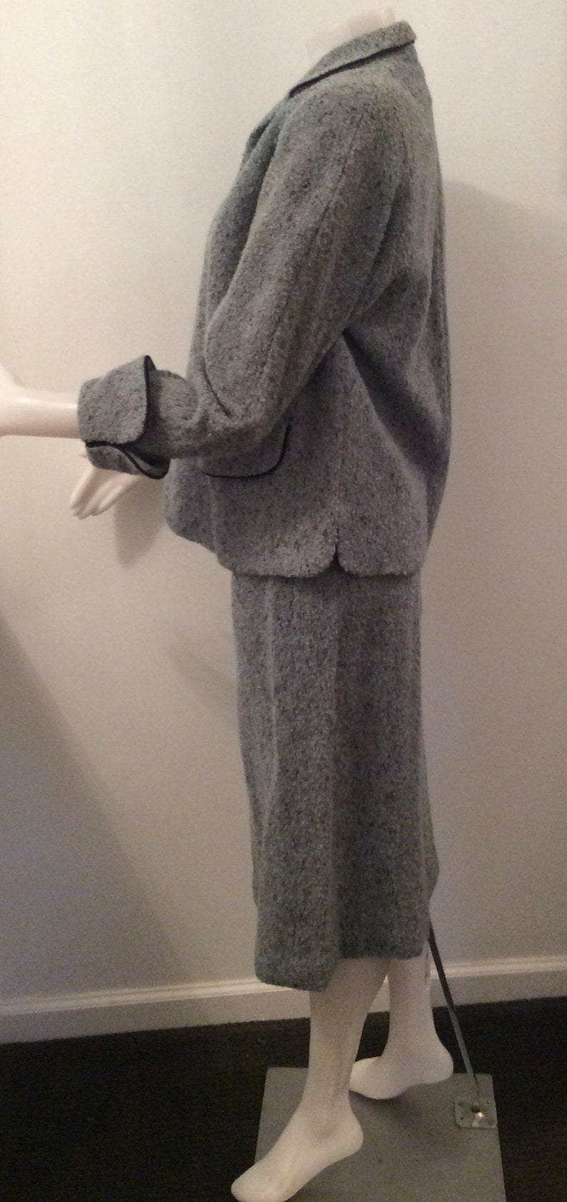 May include: A gray tweed skirt suit with black trim. The jacket has a collar and long sleeves. The skirt is knee-length.