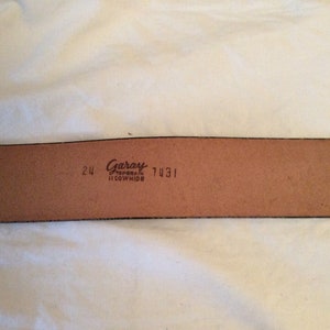 May include: A brown leather belt with the brand name "Garay" and the text "Top Grain Cowhide" printed on the inside. The belt is 24 inches wide and has the number 7431 printed on it.