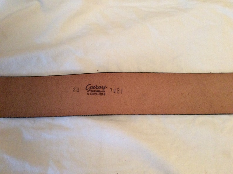 May include: A brown leather belt with the brand name "Garay" and the text "Top Grain Cowhide" printed on the inside. The belt is 24 inches wide and has the number 7431 printed on it.