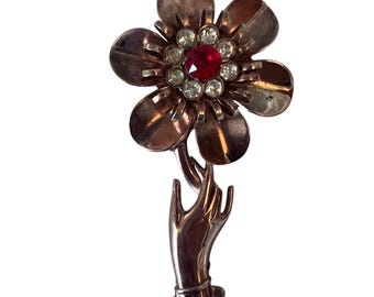 Broche vintage con una mano grande sosteniendo una flor.