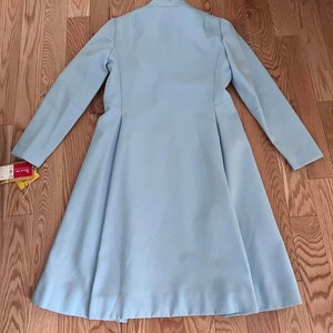May include: A light blue long-sleeved coat with a flared skirt. The coat has a simple design with a high collar and a single button closure.