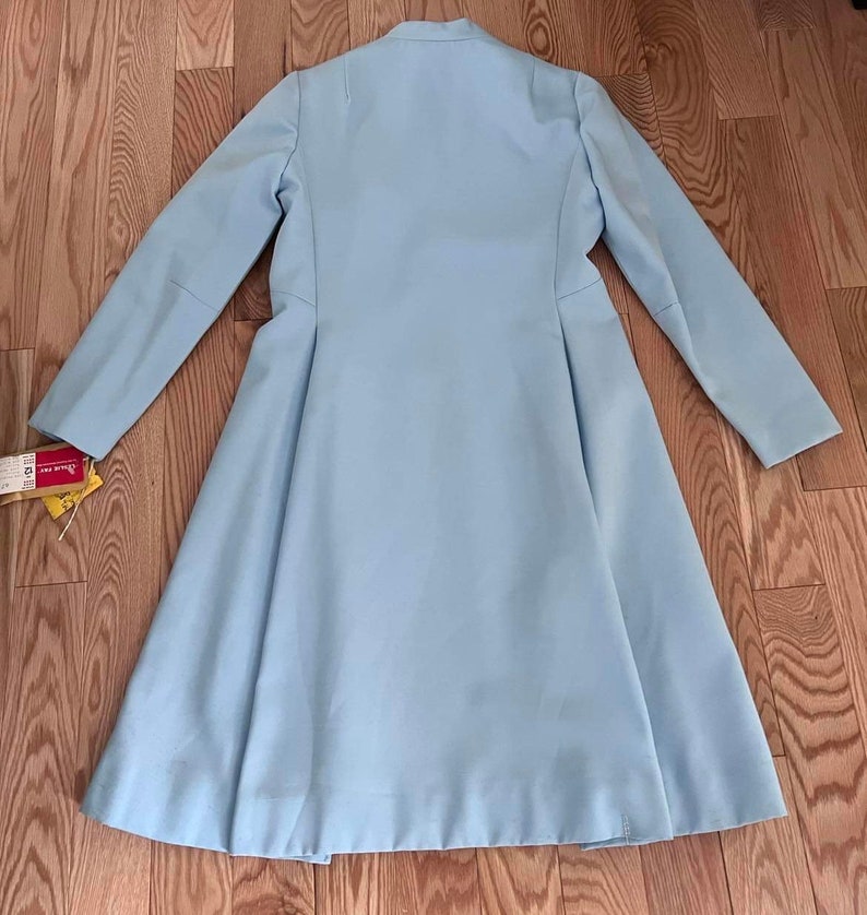 May include: A light blue long-sleeved coat with a flared skirt. The coat has a simple design with a high collar and a single button closure.