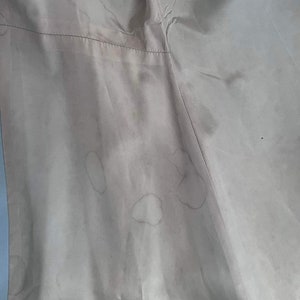 May include: A close-up of a light beige fabric with several brown stains.