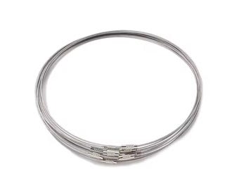 May include: A set of silver-colored bangles. The bracelets are made of thin, flexible metal and are connected with a decorative clasp. The bangles are stacked together, creating a layered look. The jewelry is displayed against a white background.