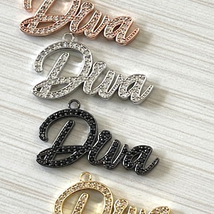 May include: Four different colored metal pendants with the word "Diva" spelled out in rhinestones. The pendants are in rose gold, silver, black, and gold.