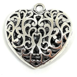 May include: Silver filigree heart charm with a delicate openwork design. The heart has a loop at the top for attaching to jewelry or other crafts.