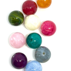 May include: Assortment of ten round, colorful, plastic beads. The beads are various shades of green, pink, purple, blue, gray, white, and orange. Some beads have a marbled or swirled pattern.