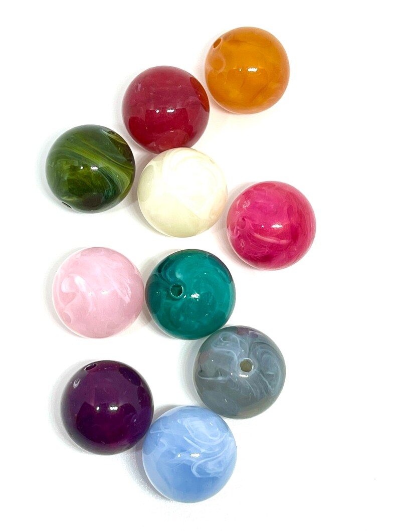 May include: Assortment of ten round, colorful, plastic beads. The beads are various shades of green, pink, purple, blue, gray, white, and orange. Some beads have a marbled or swirled pattern.
