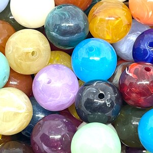 May include: A collection of colorful, round, swirl-patterned beads. The beads are made of glass or plastic and are approximately 1 inch in diameter. They are perfect for jewelry making, crafts, and home decor.