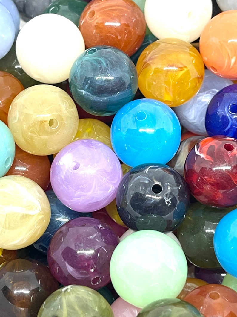 May include: A collection of colorful, round, swirl-patterned beads. The beads are made of glass or plastic and are approximately 1 inch in diameter. They are perfect for jewelry making, crafts, and home decor.