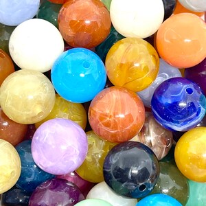 May include: A collection of colorful, round, marbled beads. The beads are made of various materials, including glass, plastic, and stone. They are all approximately 1 inch in diameter and have a smooth, polished finish.