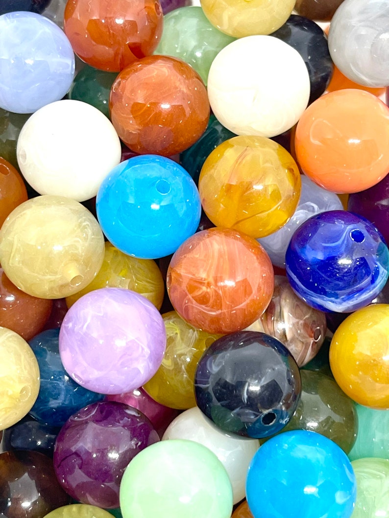 May include: A collection of colorful, round, marbled beads. The beads are made of various materials, including glass, plastic, and stone. They are all approximately 1 inch in diameter and have a smooth, polished finish.