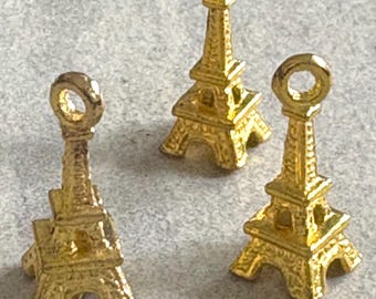 May include: Three gold-colored Eiffel Tower charms. Each charm has a loop at the top for attaching to jewelry or other crafts. The charms are detailed with the iconic tower's structure.