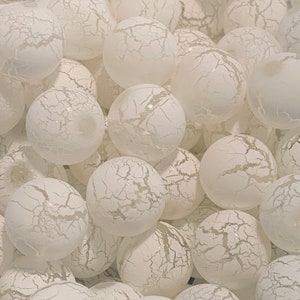 May include: A close-up of a group of white, crackled glass ornaments. The ornaments are round and have a textured surface.