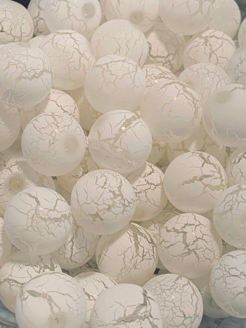 May include: A close-up of a group of white, crackled glass ornaments. The ornaments are round and have a textured surface.