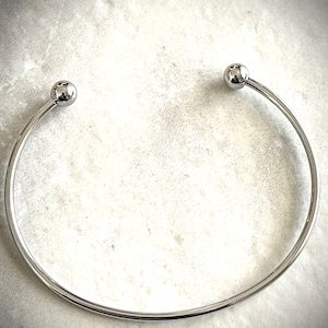 May include: A silver bangle bracelet with two round ball accents at the ends.