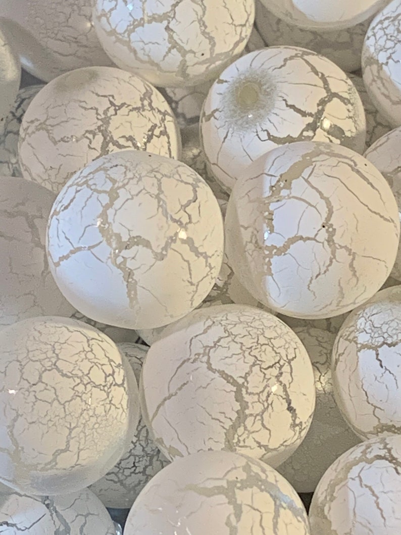 May include: A group of white glass ornaments with a crackled finish. The ornaments are round and have a subtle shimmer.