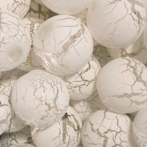 May include: A close-up of a group of white, textured, round ornaments. The ornaments have a crackled finish and are arranged in a pile.