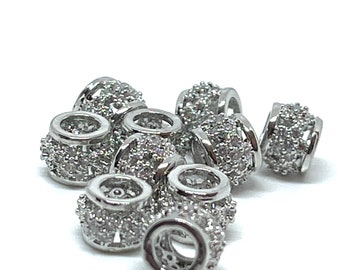 May include: A group of silver-toned metal beads with clear crystal accents. The beads are round and have a raised design.