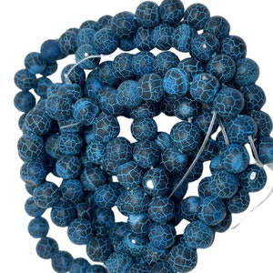 May include: A strand of blue agate beads with a crackled surface. The beads are round and have a dark blue color with white veins.