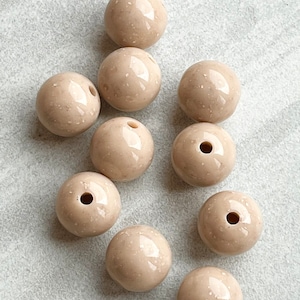 May include: Ten beige ceramic beads with a speckled finish and a hole in the center. The beads are round and smooth.