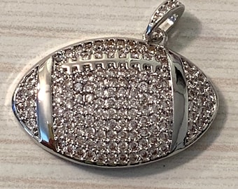 May include: A silver football pendant with a white crystal design. The pendant has a loop at the top for attaching to a chain.