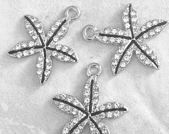 May include: Three silver starfish charms with clear crystal accents. Each charm has five points and a small loop at the top for attaching to jewelry or other crafts. The starfish are set against a light gray background.