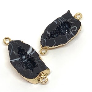May include: Two black agate stone pendant charms with gold-toned metal connector loops. The agate has a natural, raw edge and a white and black pattern.