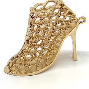 May include: A gold-colored high-heeled shoe charm with a delicate, openwork design. The shoe is made of small, interconnected circles, creating a lacy effect.