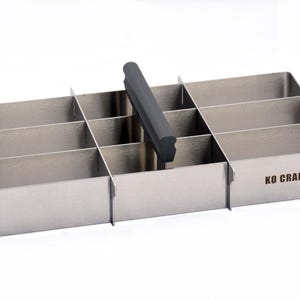 May include: A stainless steel organizer with a black handle and eight compartments. The organizer has the words "KO CRAFT" printed on the bottom.