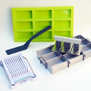 May include: A collection of soap-making tools, including a bright green silicone mold, a dark blue spatula, a stainless steel soap cutter, and a white egg slicer. These tools are designed for crafting homemade soaps.