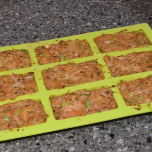 Może przedstawiać: Zielona silikonowa forma do pieczenia z dziewięcioma indywidualnymi foremkami wypełnionymi pikantną mieszanką pasztetu mięsnego. Forma znajduje się na szarym blacie.