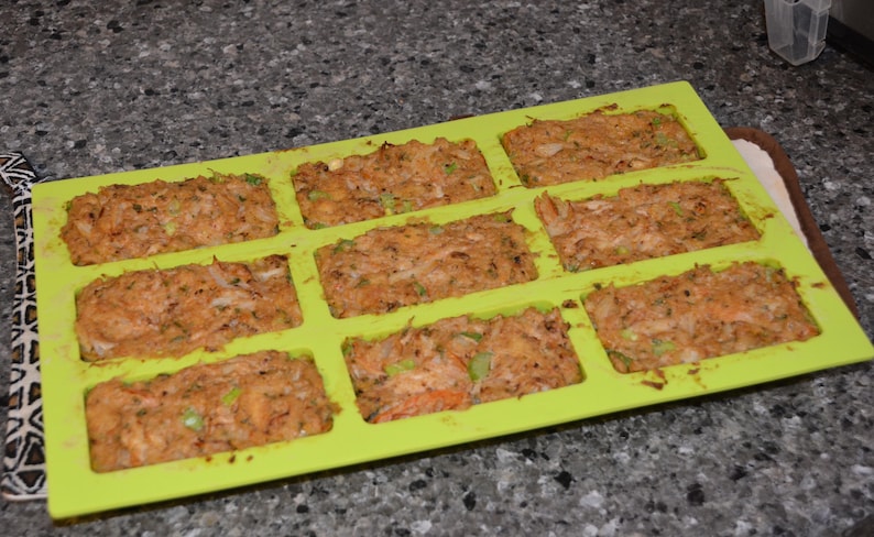 Może przedstawiać: Zielona silikonowa forma do pieczenia z dziewięcioma indywidualnymi foremkami wypełnionymi pikantną mieszanką pasztetu mięsnego. Forma znajduje się na szarym blacie.