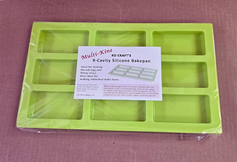 Może przedstawiać: Zielona silikonowa forma do pieczenia z dziewięcioma prostokątnymi wnękami. Forma jest oznaczona jako "Multi-KiTLE KO CRAFT'S 9-Cavity Silicone Bakepan". Jest idealna do robienia jaj Musubi i plastr&oacute;w nadzienia, a także indywidualnych wypiek&oacute;w.